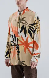 Camisa de manga larga con cuello y botones frontales, confeccionada en rayón con un estampado de hojas tropicales en tonos beige, naranja, negro y verde oliva.