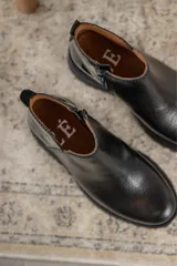 Botines negros de cuero con elástico lateral, detalle charol en el talón y suela track.