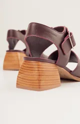 Sandalias negras de cuero con diseño minimalista y taco ancho geométrico en tono madera. La capellada lisa aporta una estética depurada y moderna, mientras que la pulsera con hebilla metálica ajustable asegura un calce firme y confortable.
