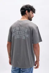 Remera de manga corta color gris oscuro con efecto lavado, corte holgado y estampado arqueado en la espalda con los nombres de ciudades: "New York", "Amsterdam" y "Boston".