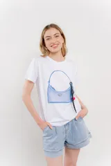 Remera blanca de algodón con estampado de un bolso con llavero colorido.