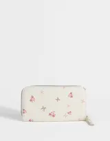 Billetera de cuerina color crema con estampado de flores y moños. Tiene formato rectangular, cierre circundante con tirador y múltiples compartimentos internos.