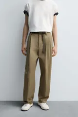 Pantalón color caqui de corte tapered relaxed fit, confeccionado en tejido de algodón. Presenta cintura con pliegues frontales dobles, bolsillos laterales en cadera y bolsillos traseros de vivo con botón. Cierre frontal con cremallera y botón.