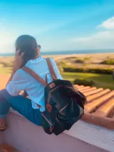 Mochila negra de cuero blando con herrajes dorados, correas marrones ajustables y cierre con cremallera.