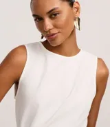 Blusa peplum blanca sin mangas con cuello redondo y ruedo asimétrico.