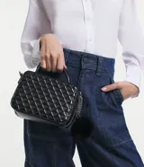 Bolso transversal tipo camera bag, color negro, hecho en material sintético texturizado. Tiene correa fina ajustable y removible, cierre por cremallera y colgante pompón.