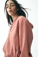 Chaqueta corta color rosa con capucha y manga larga terminada en puño. Tiene bolsillos de vivo en el delantero, bajo ajustable con cordones elásticos y cierre frontal con cremallera.