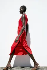 Vestido midi rojo de cuello redondo y sin mangas, con detalle de pliegues y fornitura en la cintura, y abertura frontal en el bajo.