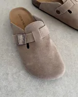 Zuecos marrones de gamuza con hebilla metálica ajustable.