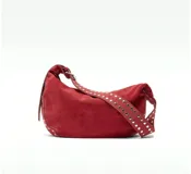 Bolso marrón de gamuza con forma de media luna y tachas plateadas. Tiene correa de hombro ajustable con hebilla metálica y cierre superior con cremallera.