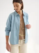 Camisa celeste de denim suave, corte relajado, con cuello clásico, cierre frontal con botones, manga larga, dos bolsillos de parche en el pecho y costuras a tono.