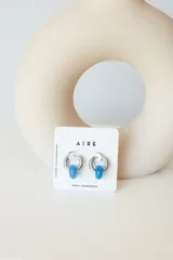 Aros de acero quirúrgico hipoalergénico con forma de argolla plateada y dije circular colgante de piedra natural color azul.