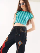 Pantalón de jean azul con parches de colores, tiro alto, corte mom-fit, apliques de cuero trenzado alrededor de los bolsillos frontales y canutillos en la parte frontal.