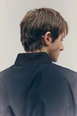 Campera bomber negra liviana con cuello elevado acanalado y cierre delantero. Tiene bolsillos laterales y un bolsillo interior, todos con cierre. Los puños y el bajo son acanalados.