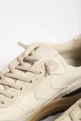 Zapatillas deportivas color beige con detalles en marrón y amarillo.