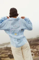 Camisa celeste de lino con botones y bordado de estrellas doradas en el pecho.