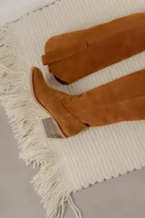 Bota alta de cuero color beige, estilo texana, con caña alta y taco bajo.