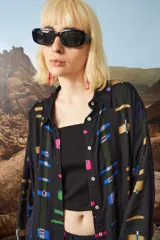 Camisa de seda con diseño gráfico en colores vibrantes sobre fondo oscuro, de corte holgado y botones en la parte frontal.