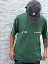 Remera oversize color verde bosque con estampado minimalista en blanco en el pecho: un globo terráqueo estilizado y el texto "STUDIO ARCHIVE".