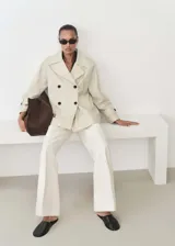 Anorak color beige con cuello de pico con solapa, manga larga con trabillas, cierre de doble botonadura y dos bolsillos laterales.