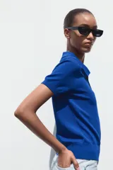 Top azul eléctrico de punto, con cuello polo, manga corta y cierre frontal con botones negros.