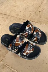 Sandalias bajas sin talón, confeccionadas en cuero negro con apliques de tachas y cuero con estampado animal print.