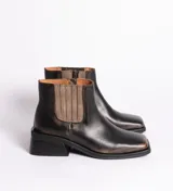 Botín de cuero negro con elásticos laterales color marrón, puntera cuadrada y taco de madera bajo. Presenta cierre lateral interno.