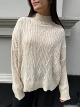 Sweater color crema de punto trenzado, con cuello alto y mangas largas.