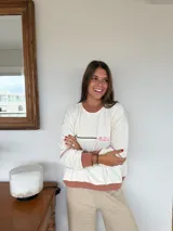 Buzo de tejido de punto color crema con cuello redondo, puños y ruedo en tono terracota. Presenta un sutil estampado de leopardo en el centro del pecho con la palabra "azu" en color fucsia.