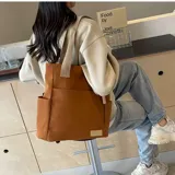 Bolso tote color marrón con asas de hombro color beige, con dos bolsillos laterales y un bolsillo frontal.
