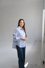 Camisa de manga larga con cuello camisero y escote en pico. Diseño a rayas verticales azules y blancas con bordados florales perforados en blanco en la parte delantera y trasera.