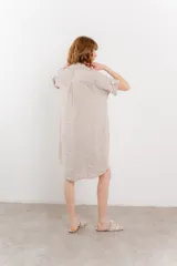 Vestido camisero corto color verde oliva, confeccionado en lino 100%. Tiene botones en la parte delantera, cuello camisero, mangas cortas con botón para arremangar y bolsillos laterales.