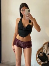 Top negro con escote drapeado, espalda descubierta y detalle de broche dorado en el hombro.