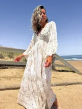 Vestido largo color crudo con estampado dorado, escote en V y mangas acampanadas.