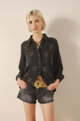 Camisa negra de tencel con bordados de canutillos, piedras, mostacillas y detalles en velvet a tono en el delantero y espalda. Tiene calce recto, manga larga, cuello camisero, puños con botón y cartera delantera con botones metálicos.