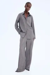 Camisa larga gris con rayas verticales finas, cuello clásico, cierre frontal de botones y mangas largas con puños abotonados.