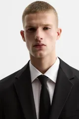 Blazer slim fit negra confeccionada en tejido con viscosa. Cuello con solapas de muesca, manga larga con puño con detalle de botones, bolsillo de vivo en pecho y de solapa en cadera, bolsillo interior, bajo con aberturas en espalda y cierre frontal con botones.