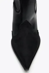Bota alta de cuero sintético negro con detalles de pespuntes en contraste y puntera de gamuza. Tiene taco fino y tiradores laterales.