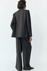 Blazer gris con diseño de líneas verticales, cuello solapa, manga larga con hombreras, bolsillos delanteros de vivo y cierre frontal cruzado con botones.