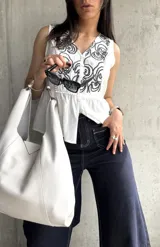 Blusa blanca sin mangas con bordado floral negro en el frente, corte evasé y cierre frontal con botones.