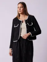 Chaqueta de tweed blanca con ribete negro, escote a la base, abertura central con botones, bolsillos delanteros y puños con aplique de botones perlados.
