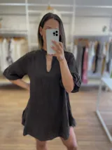 Vestido corto de lino color marrón oscuro o negro, con cuello mao con abertura en V y mangas cortas abullonadas. El calce es holgado con volados en el ruedo.