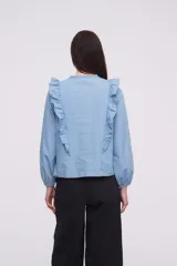 Blusa de jean azul claro, con mangas largas y detalles de volantes en el escote.
