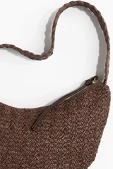 Cartera bandolera marrón de paja trenzada con correa del mismo material y cierre superior con tirador largo.