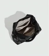 Bolso tipo hobo de cuero sintético negro con apliques de ojales metálicos plateados.