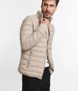 Campera puffer ultraligera color beige, con cuello alto, cierre por cremallera y bolsillos con cremallera. Incluye bolso de almacenamiento.