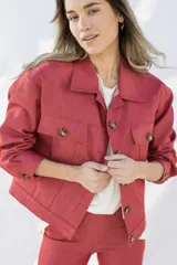 Campera color ladrillo de jean elastizado, corte cropped, con cuello camisero, cierre frontal con botones carey, bolsillos de parche con botón en el pecho y puños abotonados.