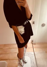 Cinturón de cuero negro con hebilla plateada y riñonera plateada con flecos.