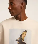 Remera overboxy color crema con estampa frontal de una mujer con un pájaro en la cabeza y lettering bordado.