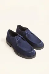 Zapato tipo wallabee de gamuza azul con costuras blancas a la vista y suela de goma negra con plataforma.